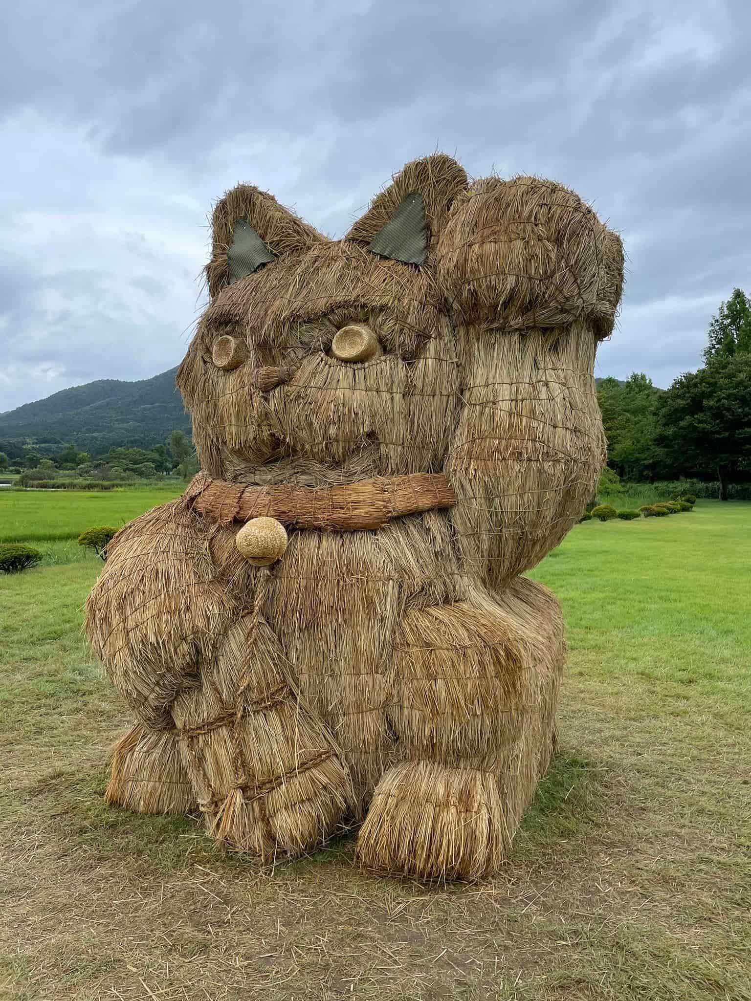 a mammoth beckoning cat sculpture made of straw